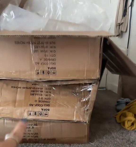 Cardboard boxes containing parts for a sofa, with text overlay "BUILDING THAT COUCH YOURSELF".