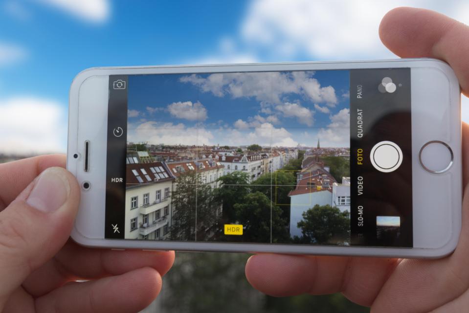 Hands holding a phone, taking a picture of a city skyline.