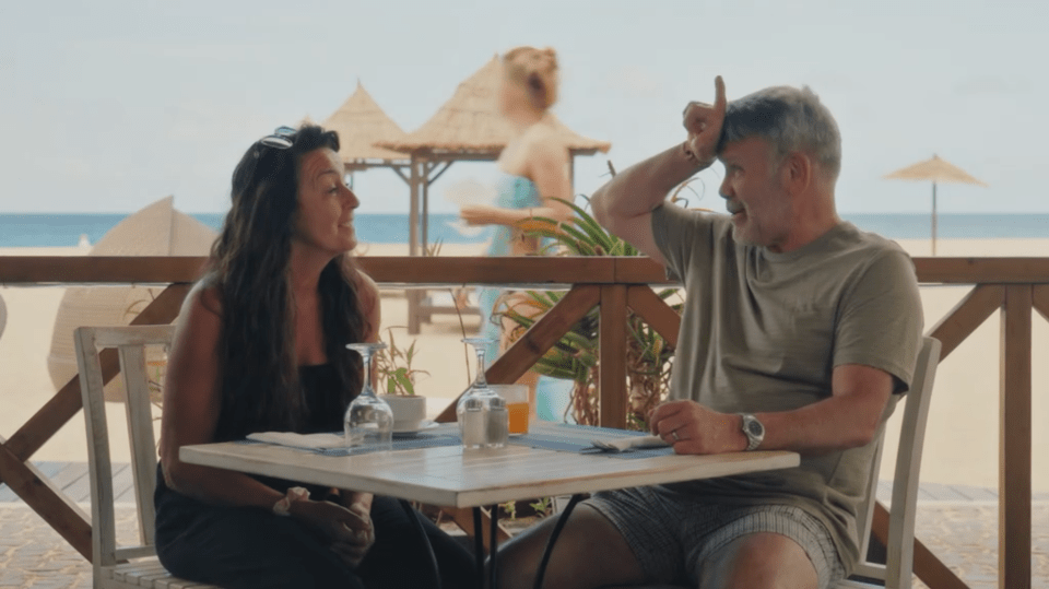 A woman and a man talking at a table in a restaurant by the beach.