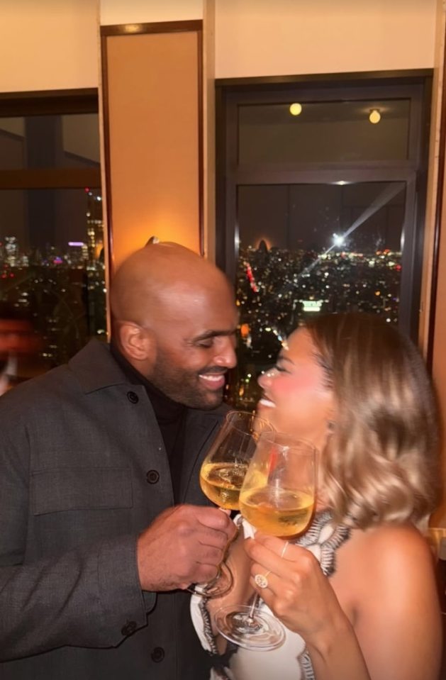 Kamie Crawford and her fiancé toasting with wine, with a city skyline visible in the background.