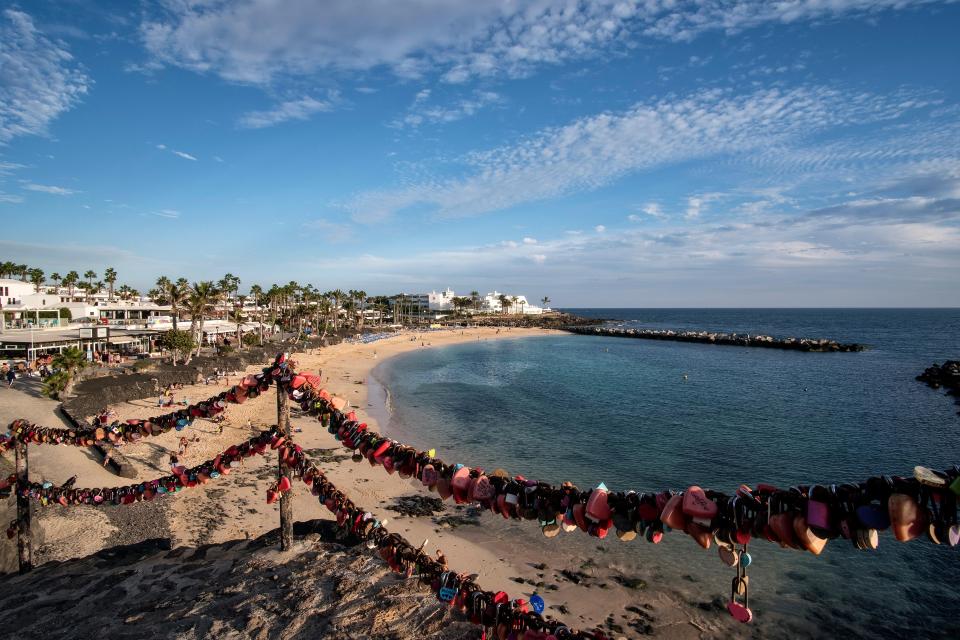 Playa Flamingo beach with a railing covered in love locks in the foreground, palm trees, and buildings along the shore.