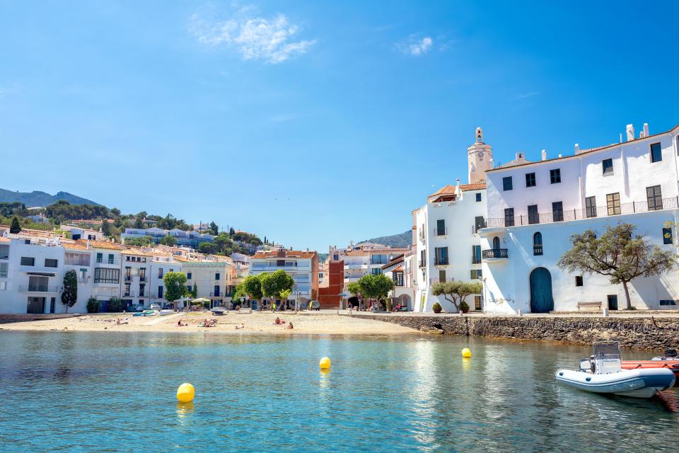 Coastal village of Cadaqués, Costa Brava, Spain with boats in the water and buildings along the beach.