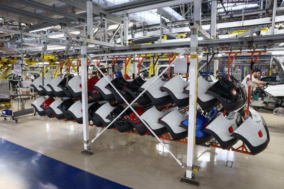 Rear car bumpers in various colors (white, red, blue, black) hanging from a production line in the Fiat Panda factory.