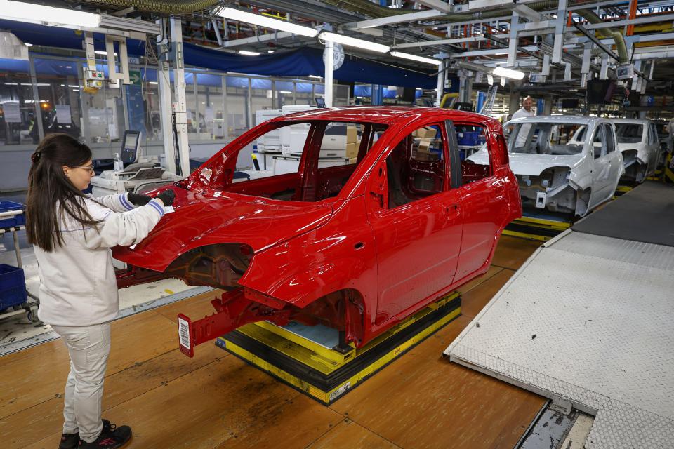 Worker inspecting the red body of a Fiat Panda on a production line.
