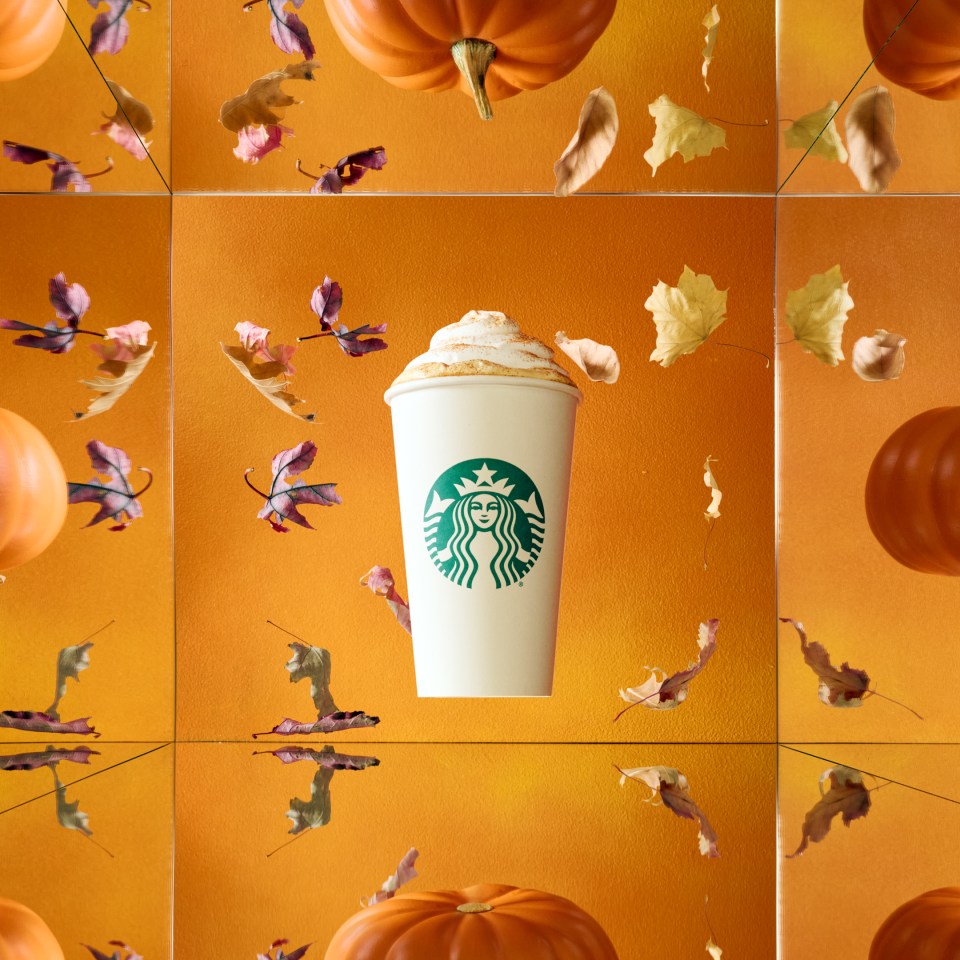 A Starbucks pumpkin spice latte with whipped cream and cinnamon surrounded by falling autumn leaves and pumpkins.