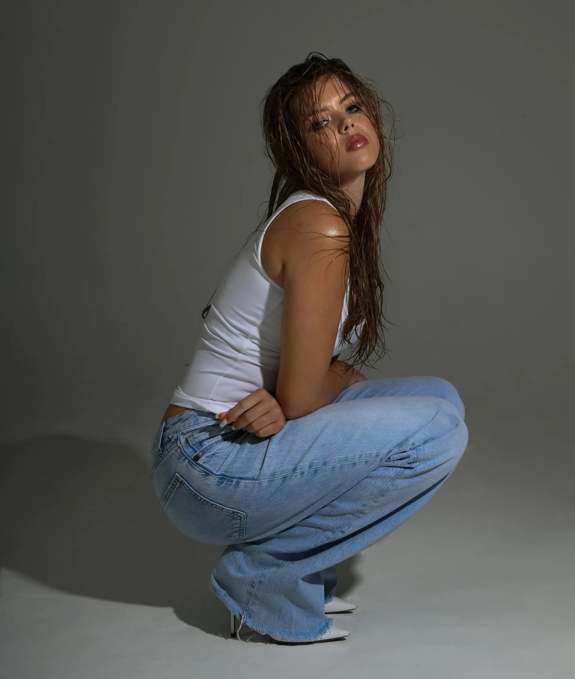 Lexie, Amanda Holden's daughter, in a photoshoot, crouching with wet hair, wearing a white tank top and blue jeans.