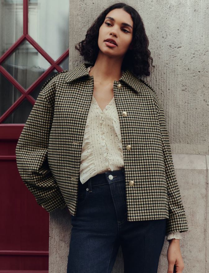 Woman wearing a black and white cropped jacket over a white blouse and dark jeans.