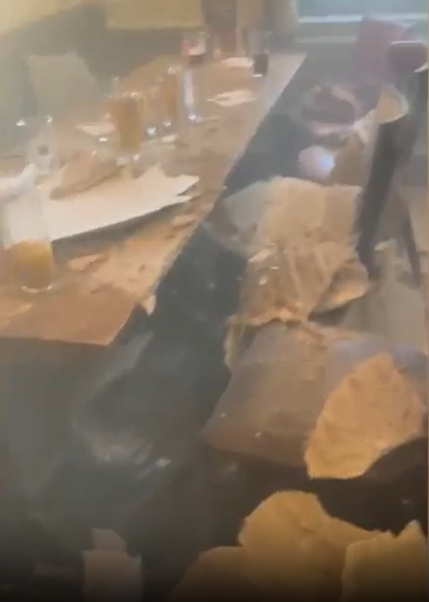 A collapsed ceiling in a dining area, with debris covering tables, drinks, and food.