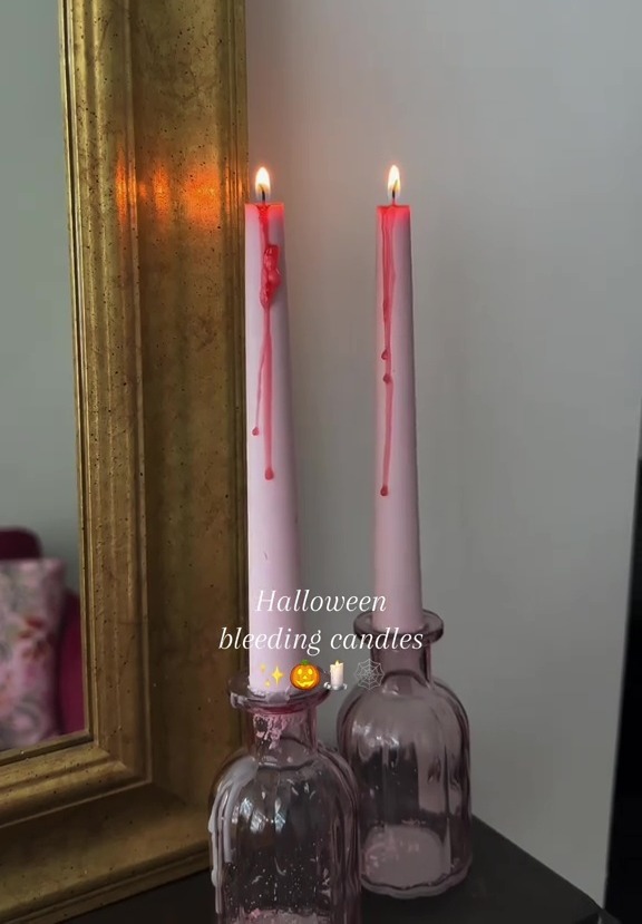 Two Halloween bleeding candles in pink holders next to a gold-framed mirror.