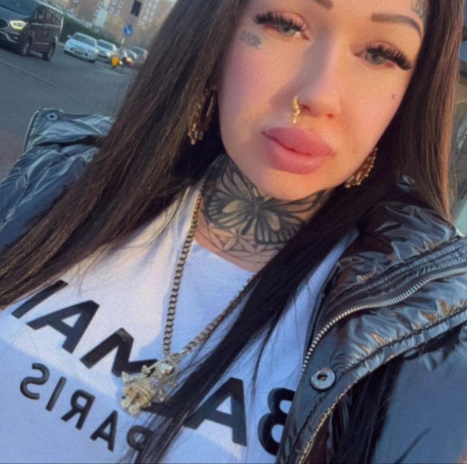 Yaz Chapman, a woman with tattoos, long dark hair, wearing a white t-shirt and a dark jacket.