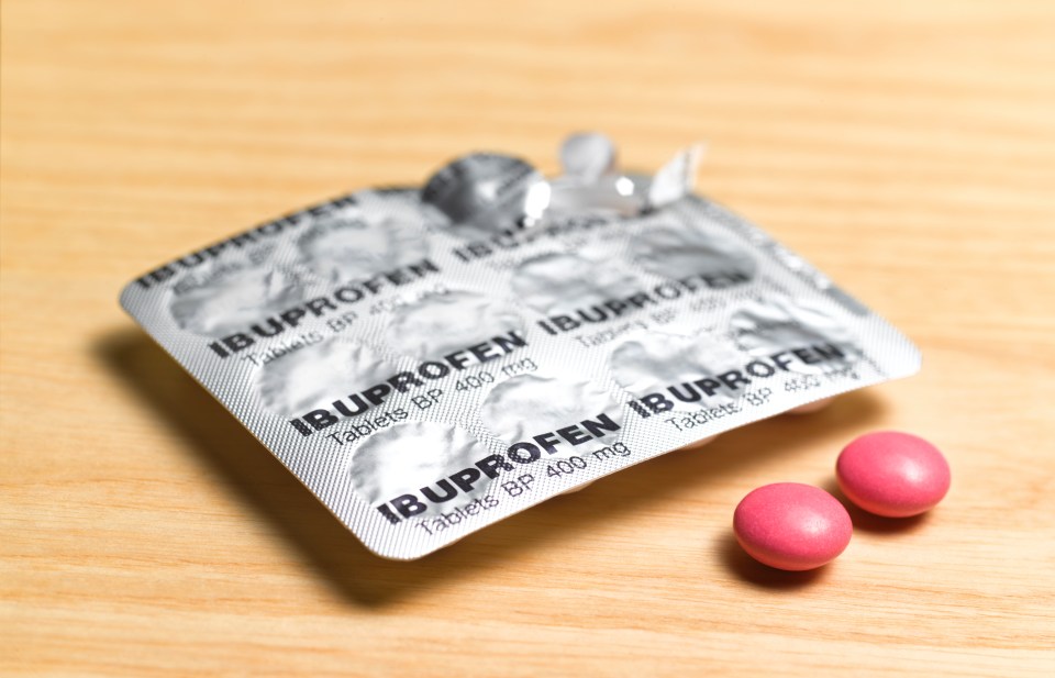 A partially used Ibuprofen blister pack and two pink Ibuprofen tablets on a light wooden surface.