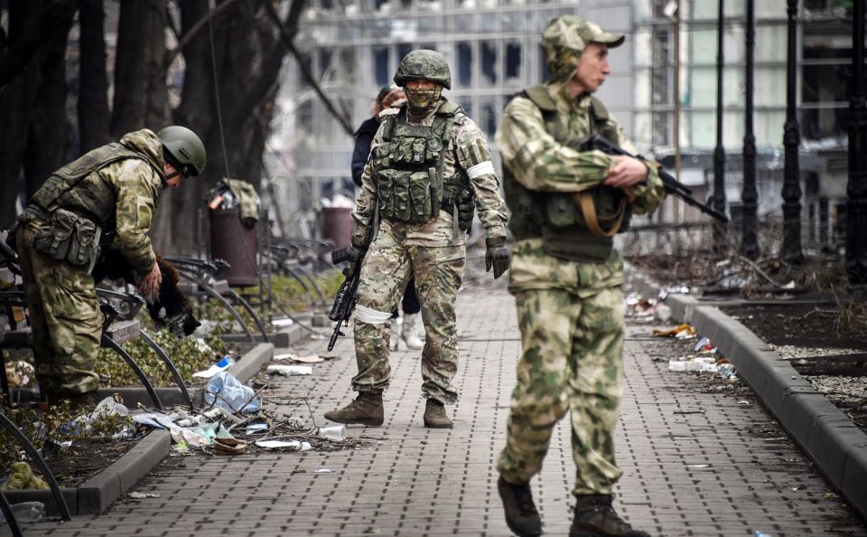 Russian soldiers walk along a street in Mariupol with one holding a cat.