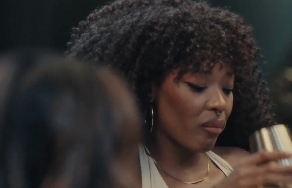 A woman with curly hair and a nose ring holds a drink shaker.