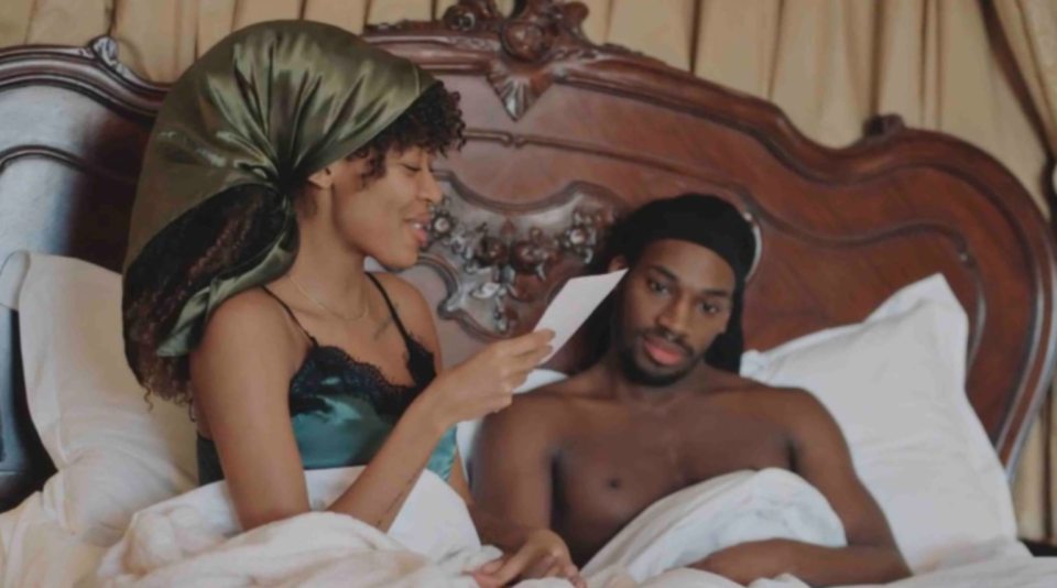 Julia Ruth and Divarni from Married at First Sight in bed, with Julia reading from a card.