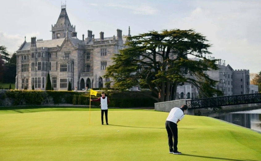 A golfer putting on a green with Adare Manor in the background.