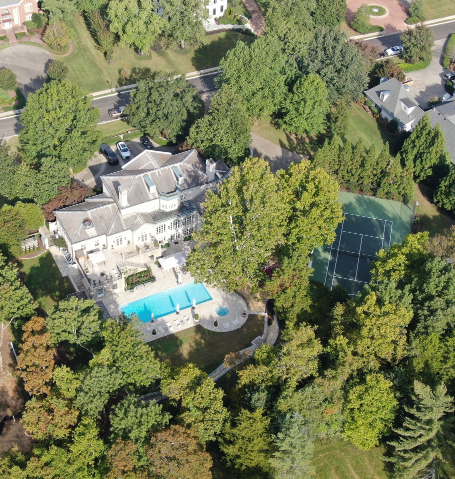Aerial view of a large estate featuring a house, swimming pool, and tennis court, surrounded by trees.