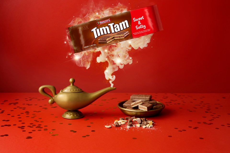 Illustration of a Sweet & Salty Tim Tam package hovering above a golden genie lamp with smoke emanating from it, on a red background with golden confetti.