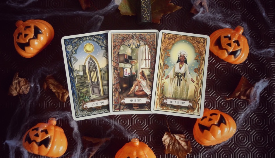 Three tarot cards, "Ace of Coins", "Six of Cups", and "Queen of Coins," surrounded by Halloween pumpkins and spiderwebs.