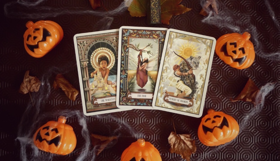 Tarot cards "The Magician", "The Fool", and "Knight of Swords" with Halloween pumpkins and spiderwebs.