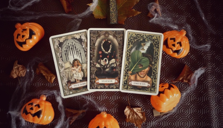 Tarot card spread of Nine of Swords, Nine of Wands, and Knight of Cups, surrounded by Halloween decorations.