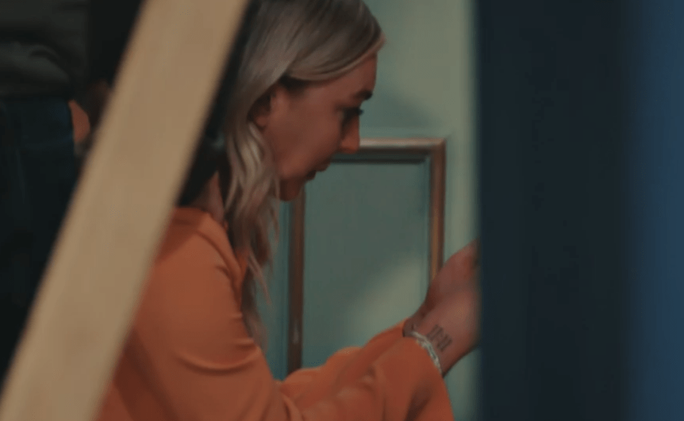 A young woman in an orange shirt looks down, holding an object in her hands.