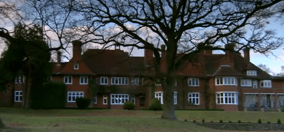 A large, red-brick house with many white-framed windows, partially obscured by a large, bare tree in the foreground.