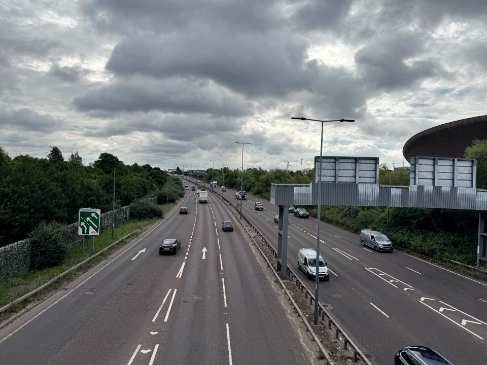 Cars and vans on a major London highway, passing through The Queen Elizabeth Olympic Park near Stratford in East London, with an overcast sky.