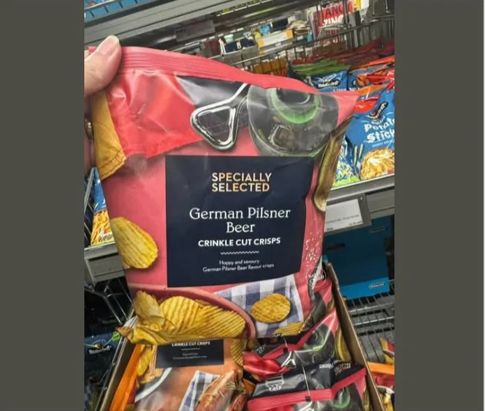 A hand holds a large bag of "Specially Selected German Pilsner Beer Crinkle Cut Crisps" in an Aldi store.
