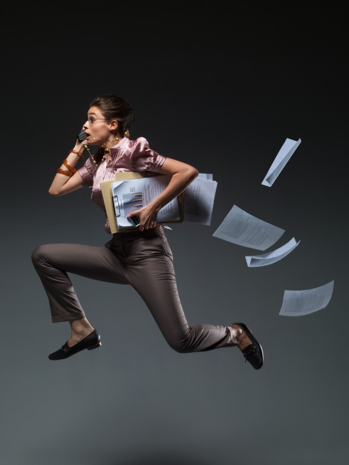 Businesswoman leaping through the air, phone to her ear, carrying files and papers.