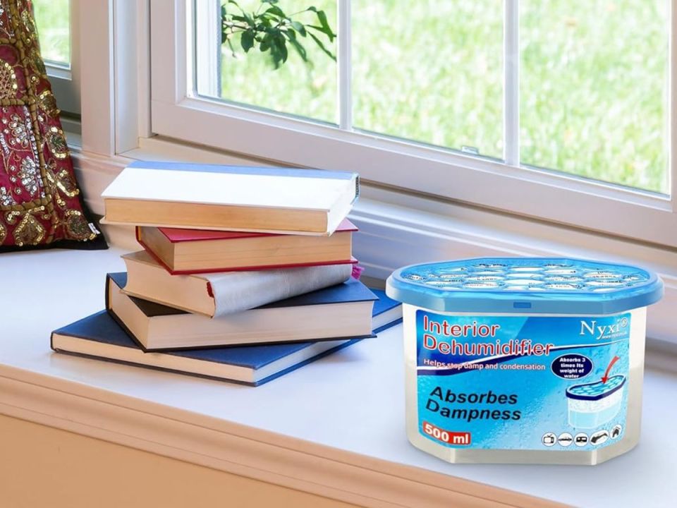 A Nyxi Interior Dehumidifier next to a stack of books on a windowsill.