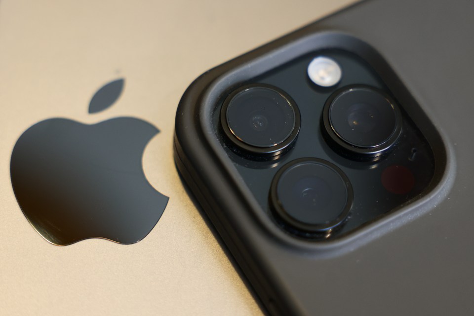 Close-up of Apple logo on a MacBook and the camera array of an iPhone 16 Pro.