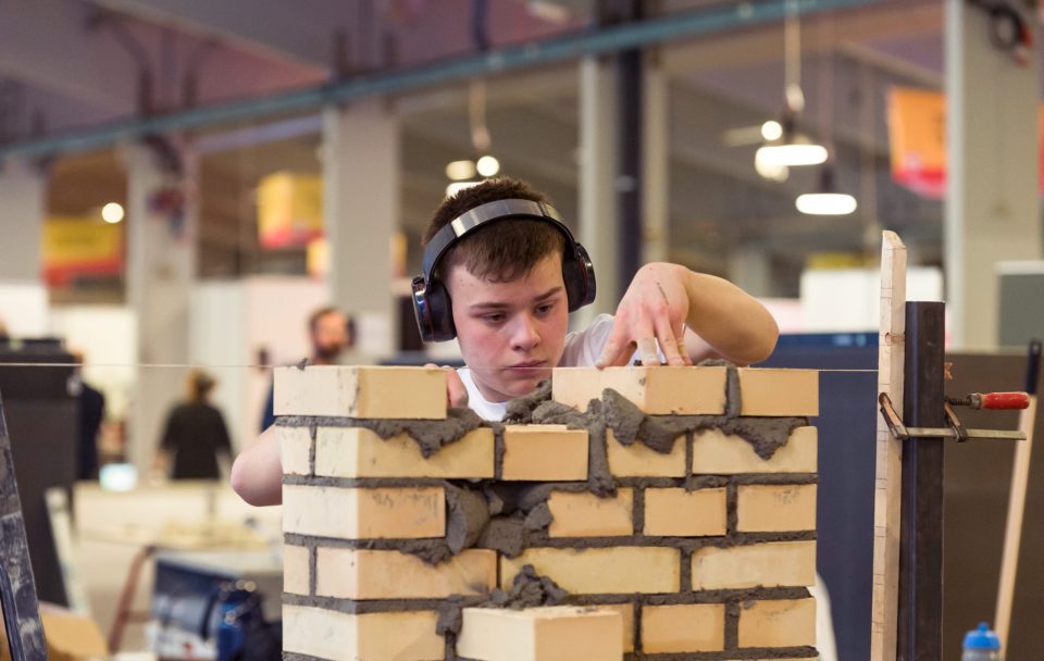 A young man wearing headphones carefully places bricks into a wall.
