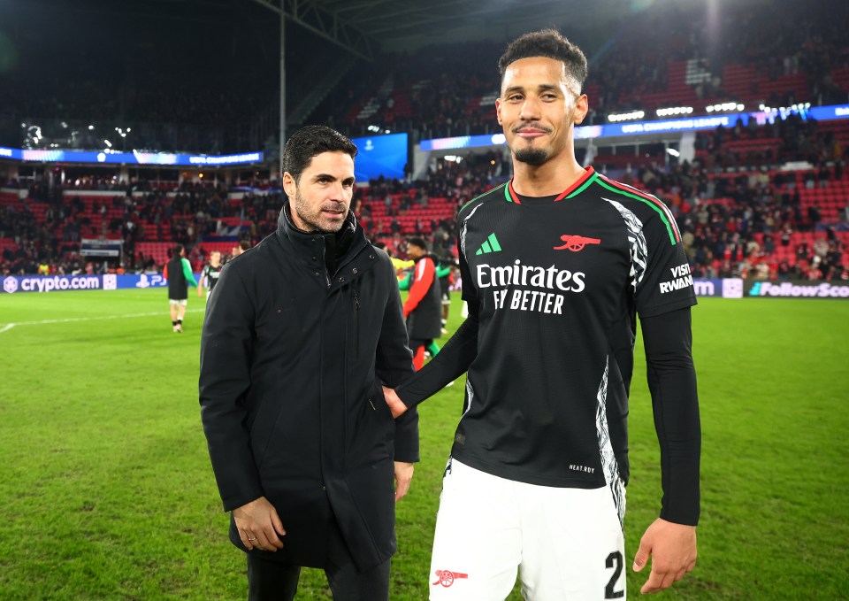 Arsenal manager Mikel Arteta and player William Saliba on the field celebrating victory at a UEFA Champions League match.