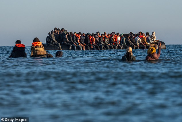 Migrants wade into the sea to board a dinghy to cross the English Channel on August 25, 2025