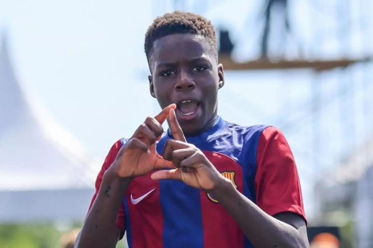 Young male soccer player in a blue and red jersey making a hand gesture.