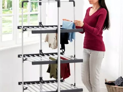 Person placing clothes on a three-tiered drying rack.