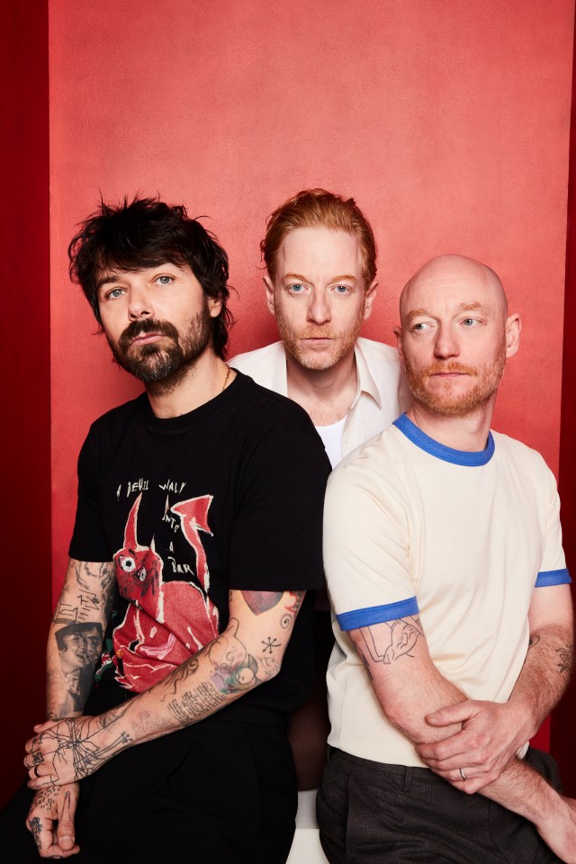 Biffy Clyro band members, Simon Neil, James Johnston, and Ben Johnston, posing in front of a red background.