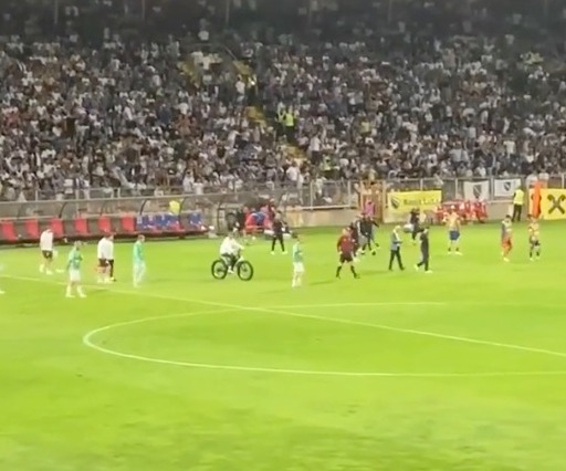 A person on a bicycle rides across a soccer field during a game.