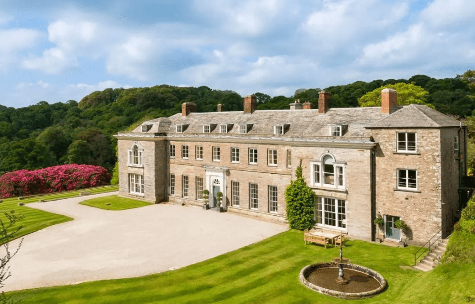 Large stone manor house with manicured lawn and fountain.