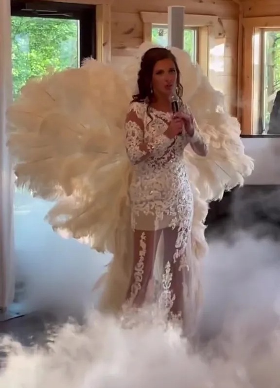 Bride lip-syncing at wedding reception in a feathered, sheer dress.