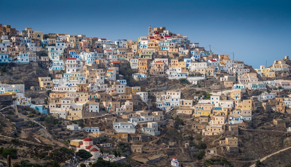 View of the ancient village of Olympos, Karpathos, Greece, with colorful houses built into a hillside under a clear blue sky.
