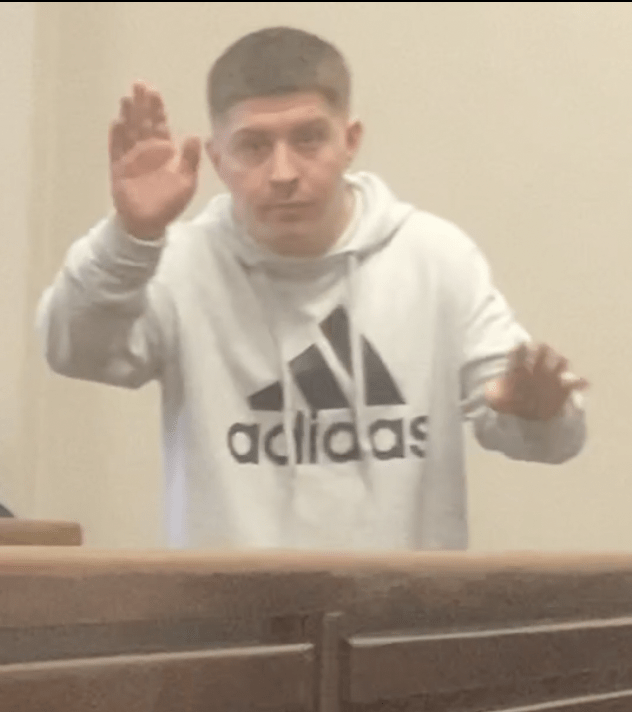 Man in a white Adidas hoodie raising his hand in a magistrates court.