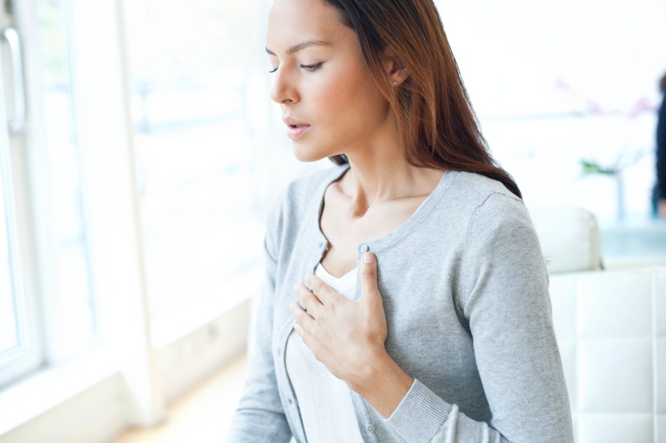 Young woman with her hand on her chest, looking down.