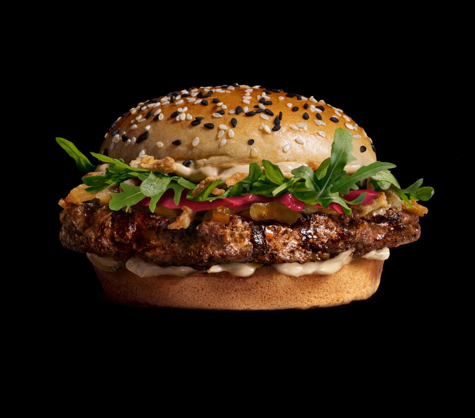 Wagyu burger on a sesame seed bun with arugula and caramelized onions.