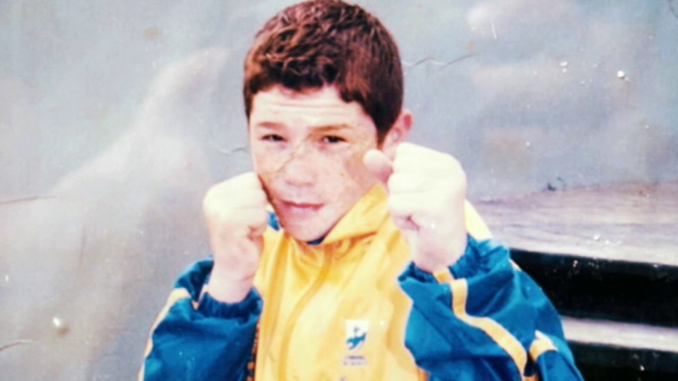Young boy in a yellow and blue jacket, boxing stance.