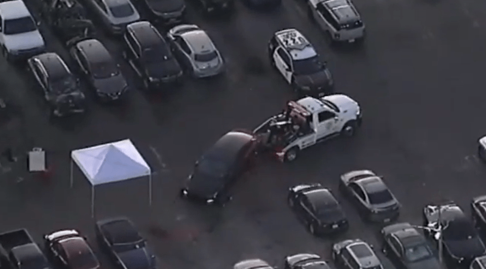 Aerial view of a car being towed in a parking lot with a police car and a white tent nearby.