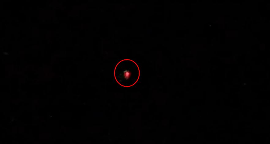 A small blurry red object in the center of a black background, circled in red.