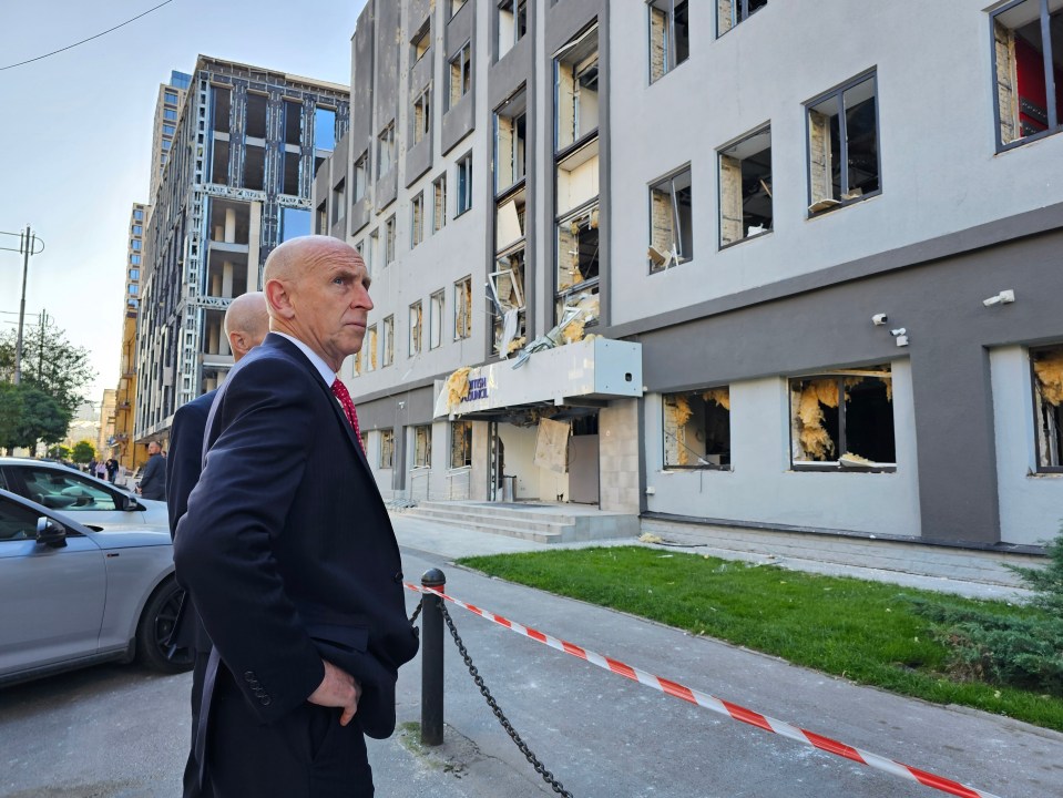 A man in a suit stands before a bomb-damaged building in Kyiv.