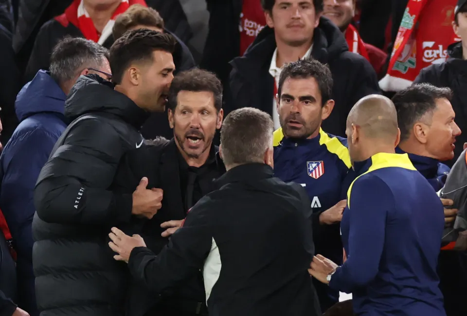 Diego Simeone being restrained by staff during a football match.