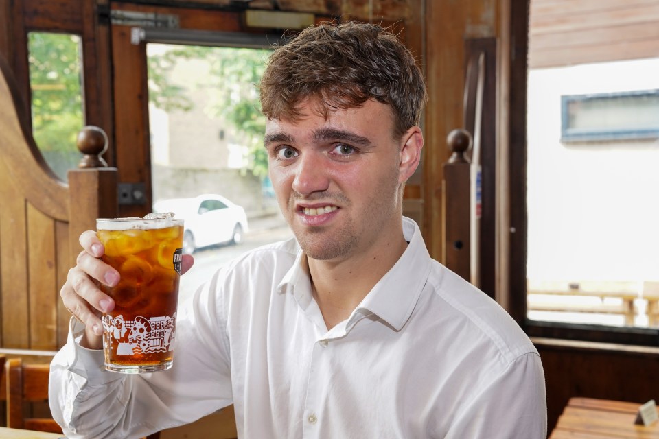Man in a white shirt holding a pint of beer with ice.
